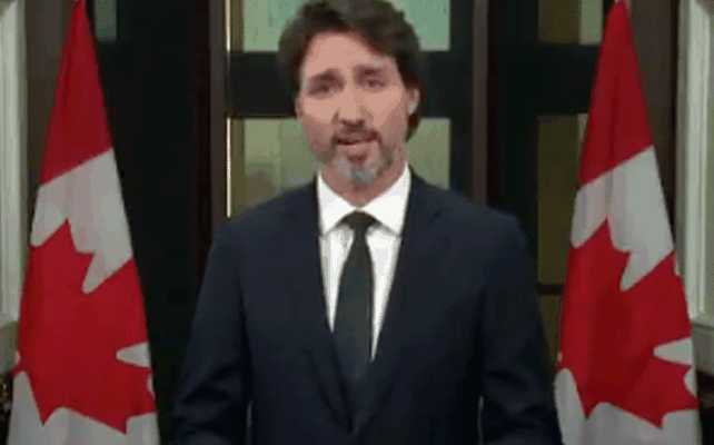 Trudeau in front of Canada Flags speaking to the camera